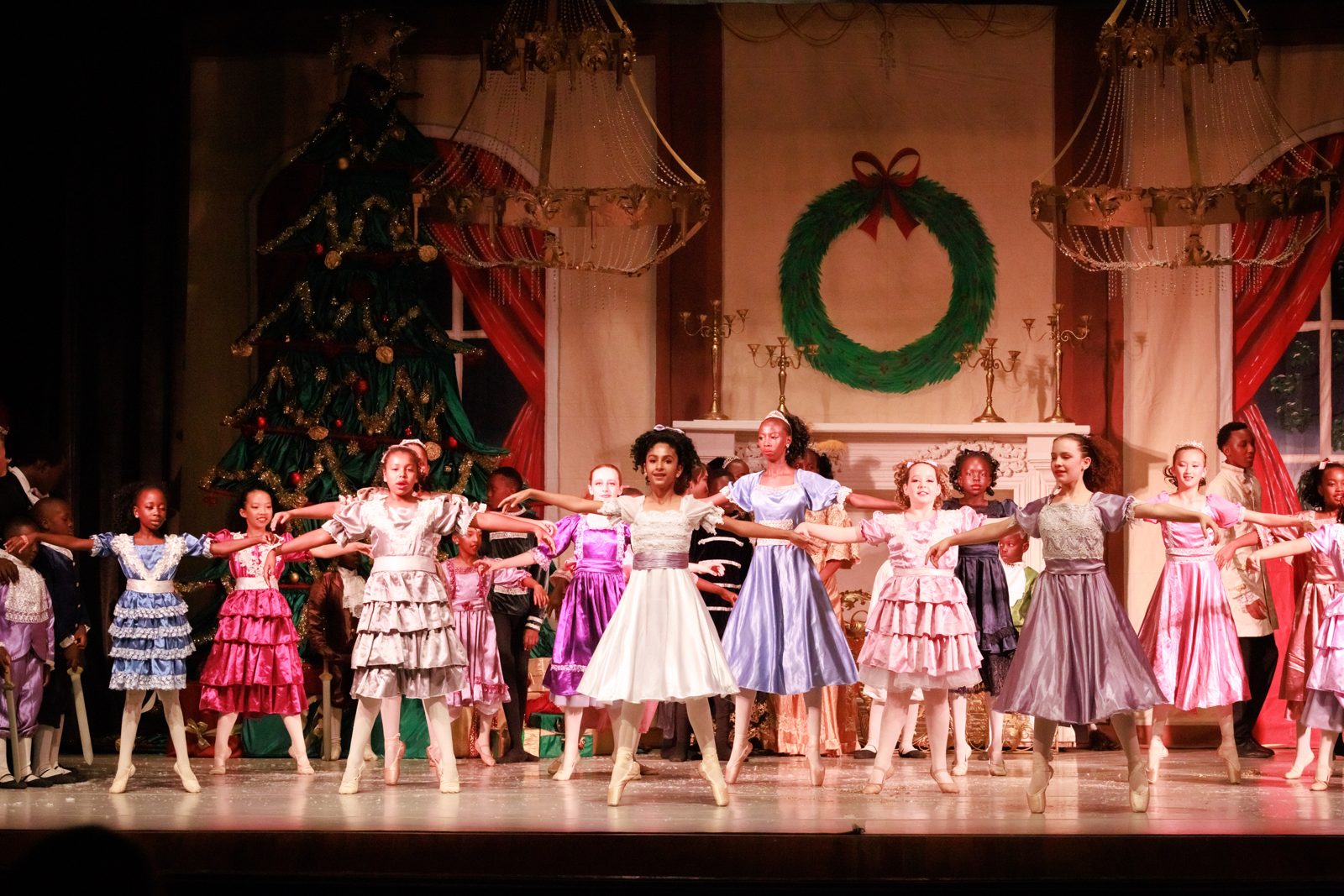 Young dancers in pastel party dresses dancing in front of a Christmas tree and wreath